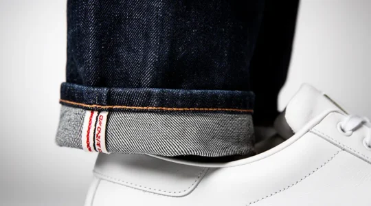 Détail rapproché d'un jean brut indigo foncé à côté de baskets blanches immaculées sur fond minimaliste