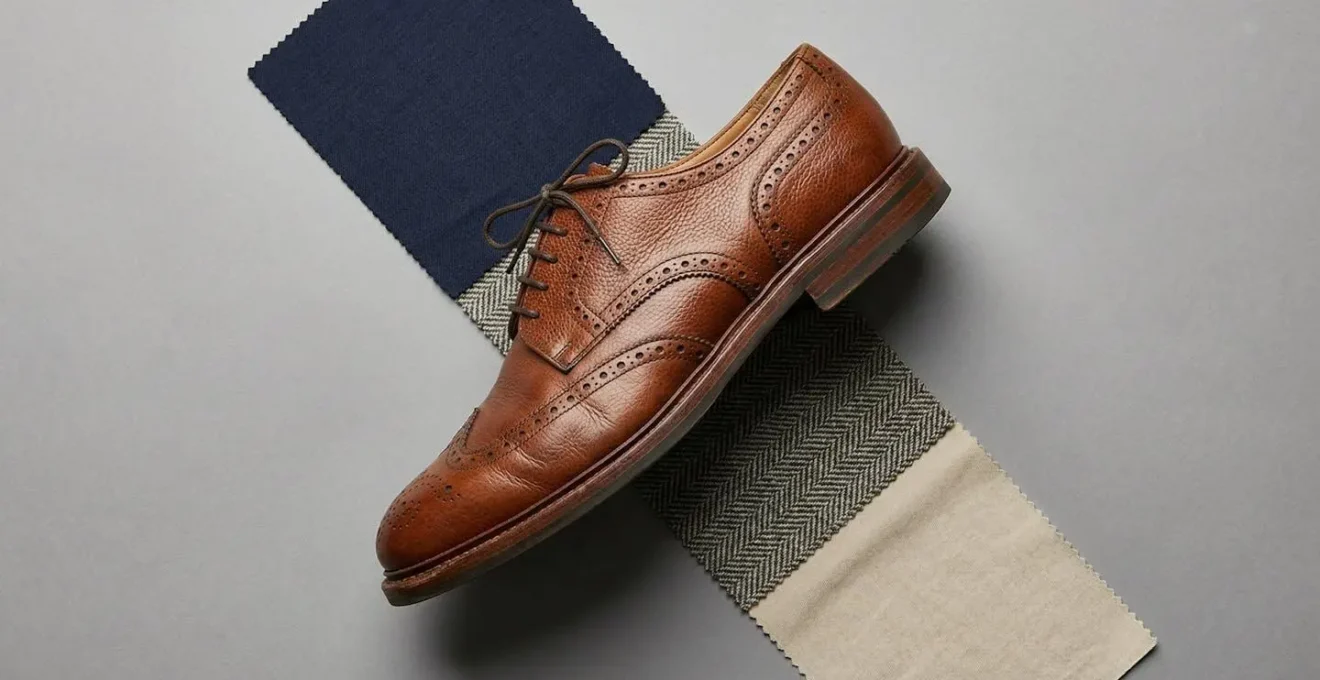 Composition minimaliste montrant une brogue en cuir grainé avec des échantillons de tissus unis et texturés